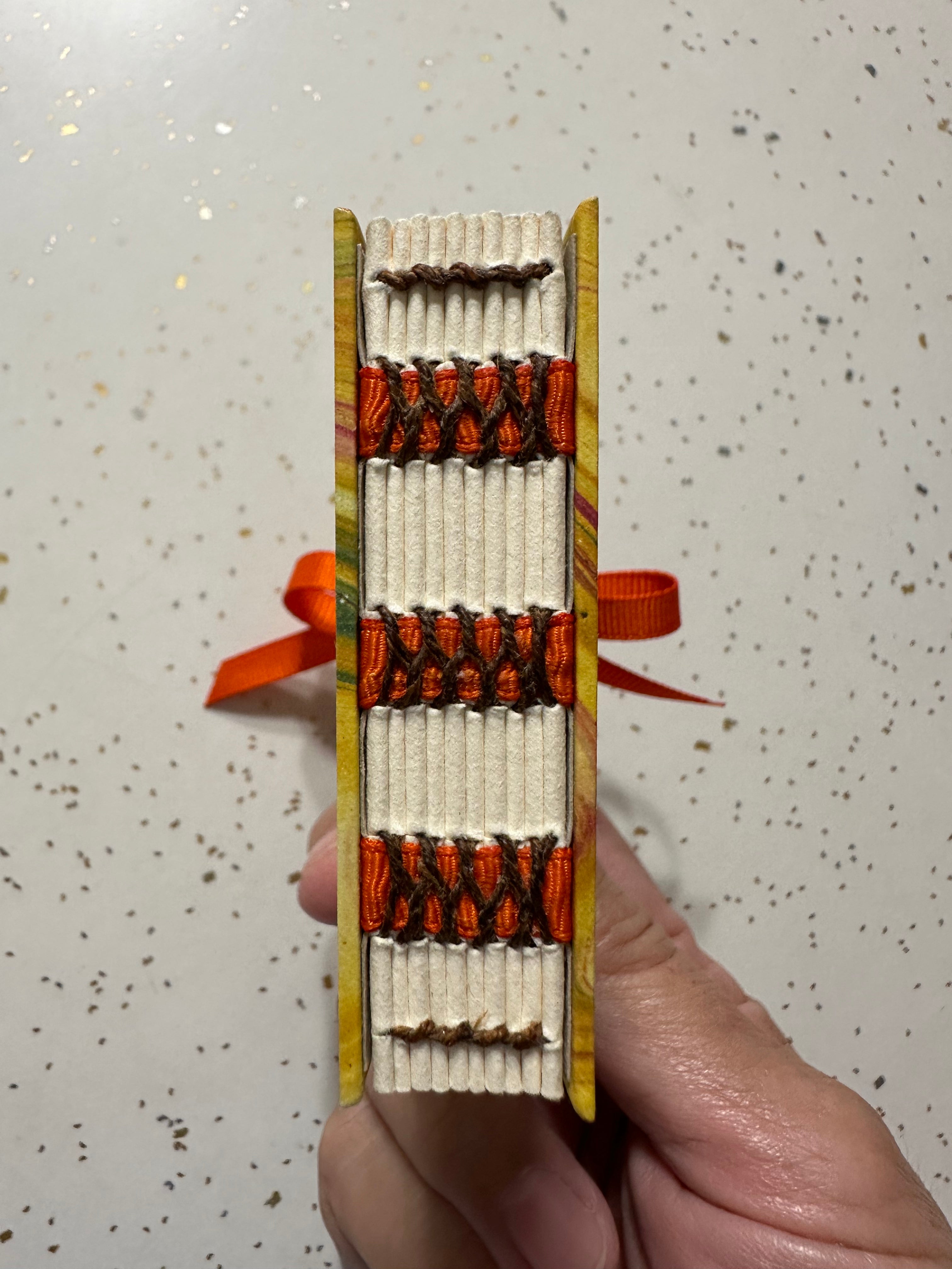 Hand holding a small, intricately miniature bound book so the spine is visable.