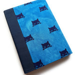 A handbound card covered in blue fabric with black cat faces peeking from the dges, complemented by a deep blue cloth spine - a whimsical and thoughtful keepsake card