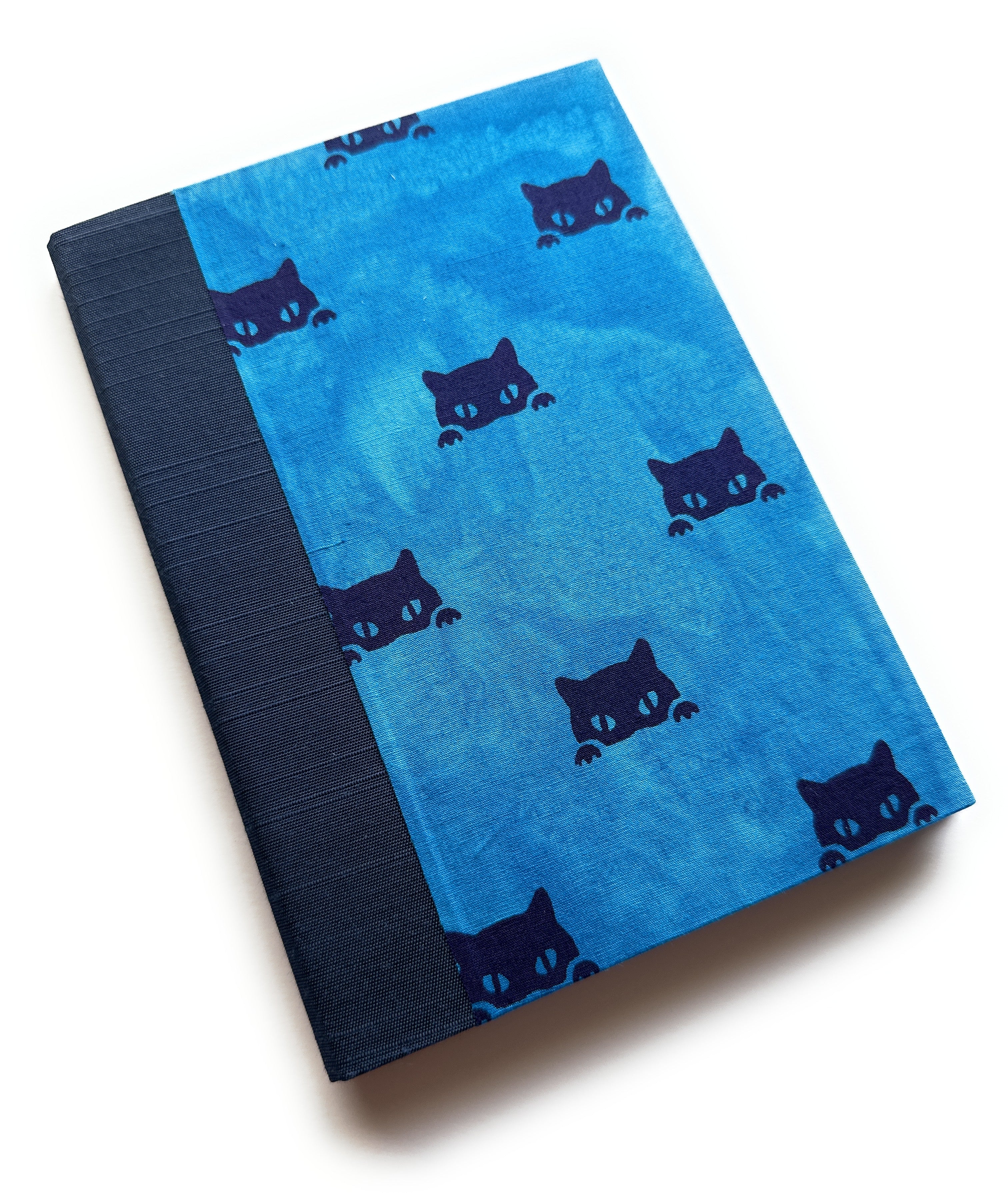 A handbound card covered in blue fabric with black cat faces peeking from the dges, complemented by a deep blue cloth spine - a whimsical and thoughtful keepsake card