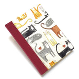 This handmade journal features a delightful fabric cover adorned with playful illustrated cats in various poses, making it a perfect notebook for cat lovers. Bound with a durable red spine and filled with high-quality blank pages, it's an ideal choice for journaling, sketching, or note-taking with a touch of feline charm.