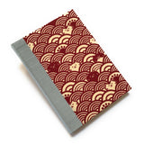 This handcrafted cat journal features a unique red and beige fabric cover with a Japanese wave pattern intertwined with whimsical feline faces. The blue gray bookbinding cloth covers the spine and is Ideal for cat lovers and stationery enthusiasts, this artisan notebook adds charm to any collection.