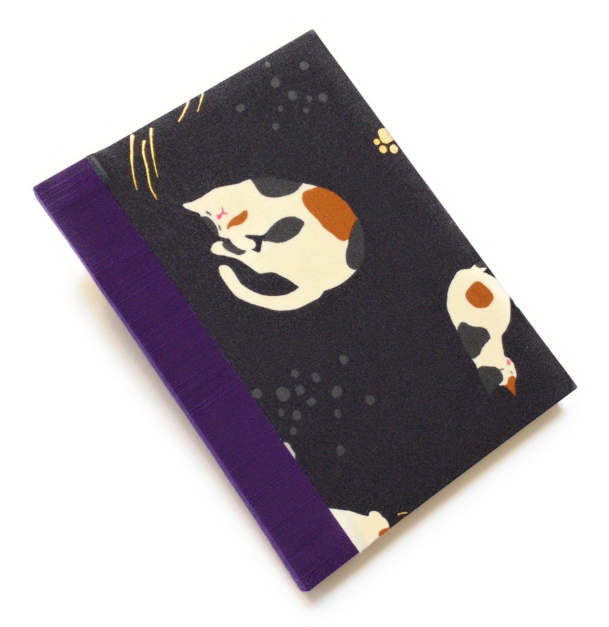 This handmade journal features a black fabric cover adorned with a serene sleeping calico cat design. Bound with a sturdy purple bookbinding cloth, this notebook is perfect for journaling, sketching, or note-taking.