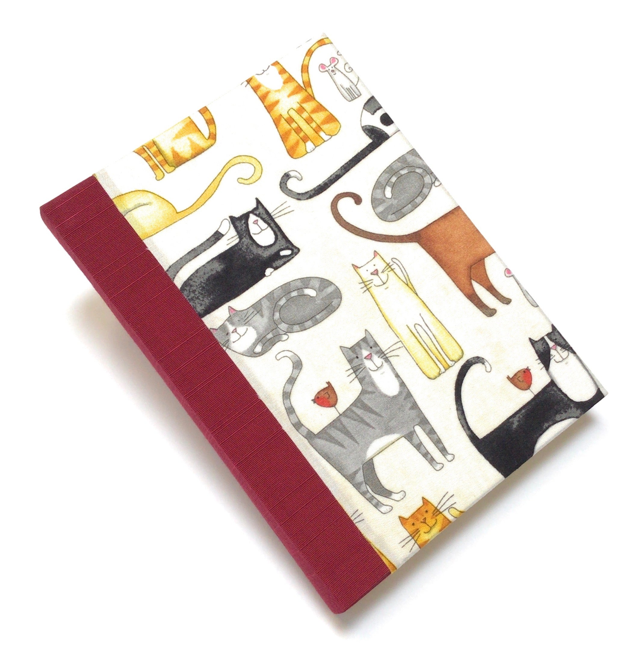 This handmade journal features a delightful fabric cover adorned with playful illustrated cats in various poses, making it a perfect notebook for cat lovers. Bound with a durable red spine and filled with high-quality blank pages, it's an ideal choice for journaling, sketching, or note-taking with a touch of feline charm.