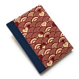 This handcrafted cat journal features a unique red and beige fabric cover with a Japanese wave pattern intertwined with whimsical feline faces. The dark blue  bookbinding cloth covers the spine and is Ideal for cat lovers and stationery enthusiasts, this artisan notebook adds charm to any collection.