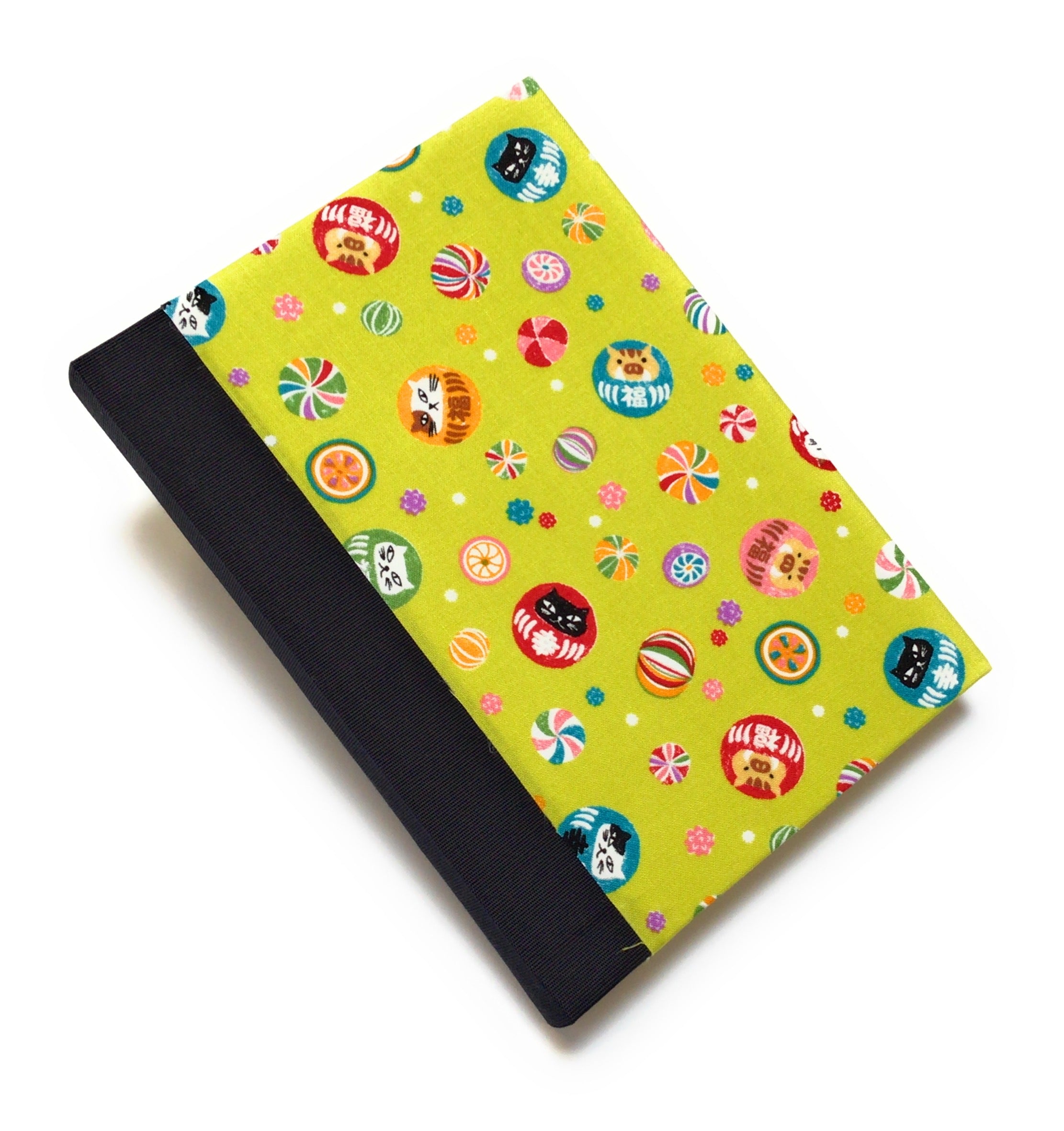 This handmade journal features a lively Japanese-inspired fabric cover adorned with lucky Daruma dolls, playful cat illustrations, and vibrant temari balls on a striking green background. The durable black spine adds contrast, making it a perfect notebook for journaling, sketching, or note-taking. Designed for cat lovers and fans of Japanese aesthetics, this unique handcrafted journal is a stylish and functional keepsake.