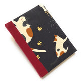 This handmade journal features a black fabric cover adorned with a serene sleeping calico cat design. Bound with a sturdy red bookbinding cloth, this notebook is perfect for journaling, sketching, or note-taking.
