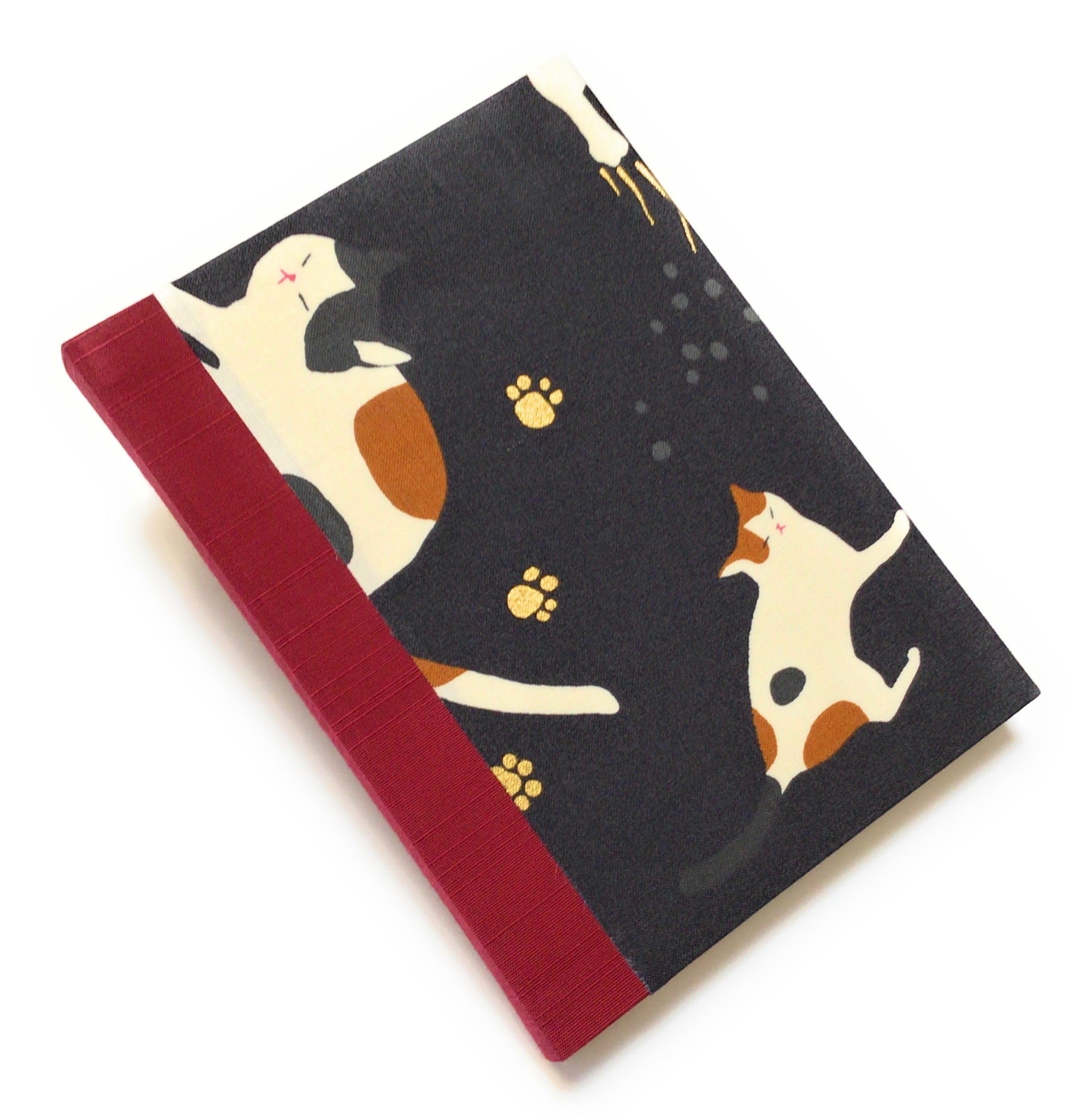 This handmade journal features a black fabric cover adorned with a serene sleeping calico cat design. Bound with a sturdy red bookbinding cloth, this notebook is perfect for journaling, sketching, or note-taking.