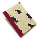 This handcrafted journal features a charming beige fabric cover adorned with playful black tuxedo cats and delicate gold paw prints. The red spine adds a natural touch, creating a timeless design perfect for cat lovers, writers, and artists. With high-quality binding and a unique Japanese-inspired aesthetic, this cat-themed notebook makes an excellent gift for journaling, sketching, or daily notes.