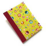 This handmade journal features a lively Japanese-inspired fabric cover adorned with lucky Daruma dolls, playful cat illustrations, and vibrant temari balls on a striking green background. The durable red spine adds contrast, making it a perfect notebook for journaling, sketching, or note-taking. Designed for cat lovers and fans of Japanese aesthetics, this unique handcrafted journal is a stylish and functional keepsake.