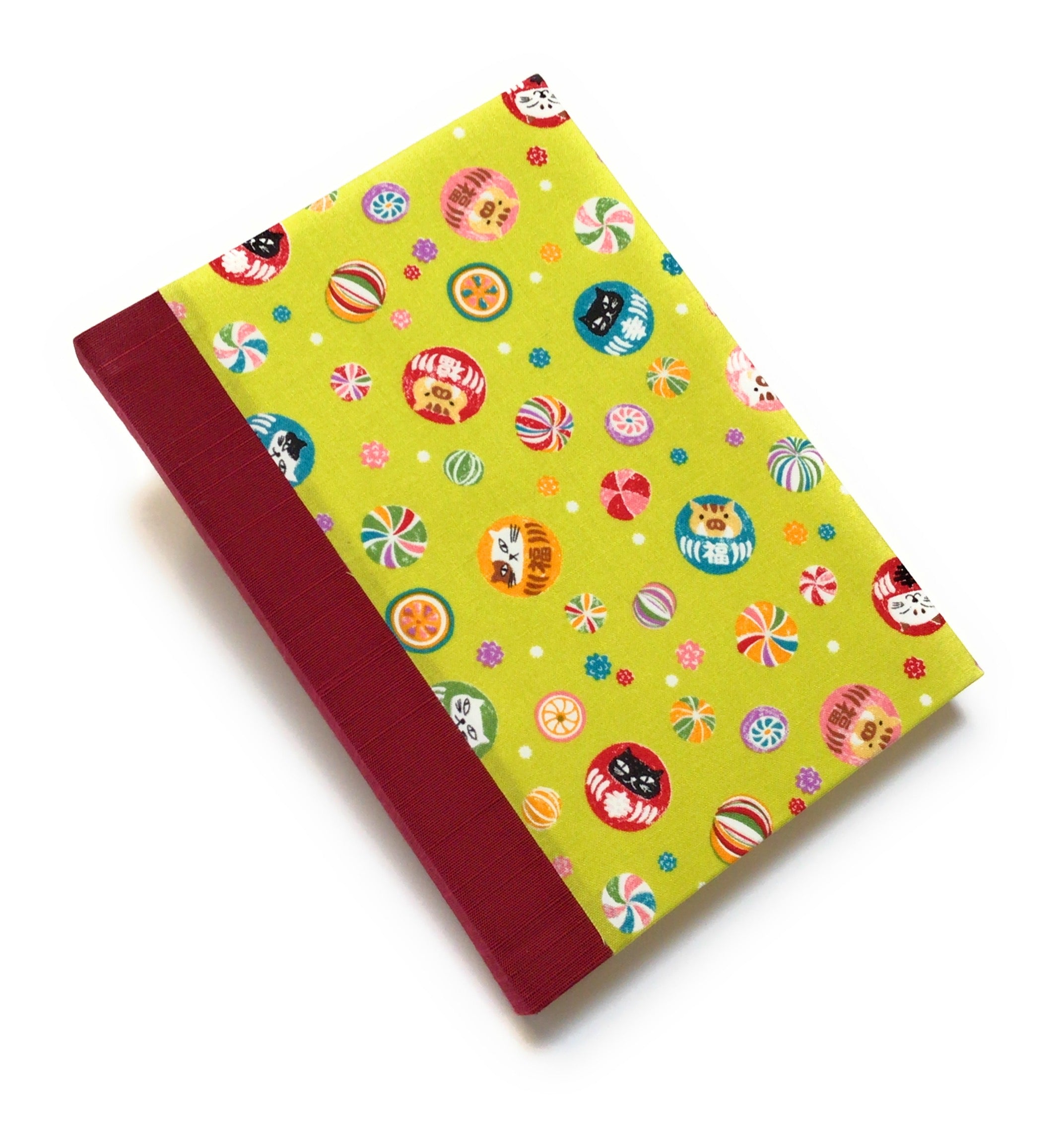 This handmade journal features a lively Japanese-inspired fabric cover adorned with lucky Daruma dolls, playful cat illustrations, and vibrant temari balls on a striking green background. The durable red spine adds contrast, making it a perfect notebook for journaling, sketching, or note-taking. Designed for cat lovers and fans of Japanese aesthetics, this unique handcrafted journal is a stylish and functional keepsake.