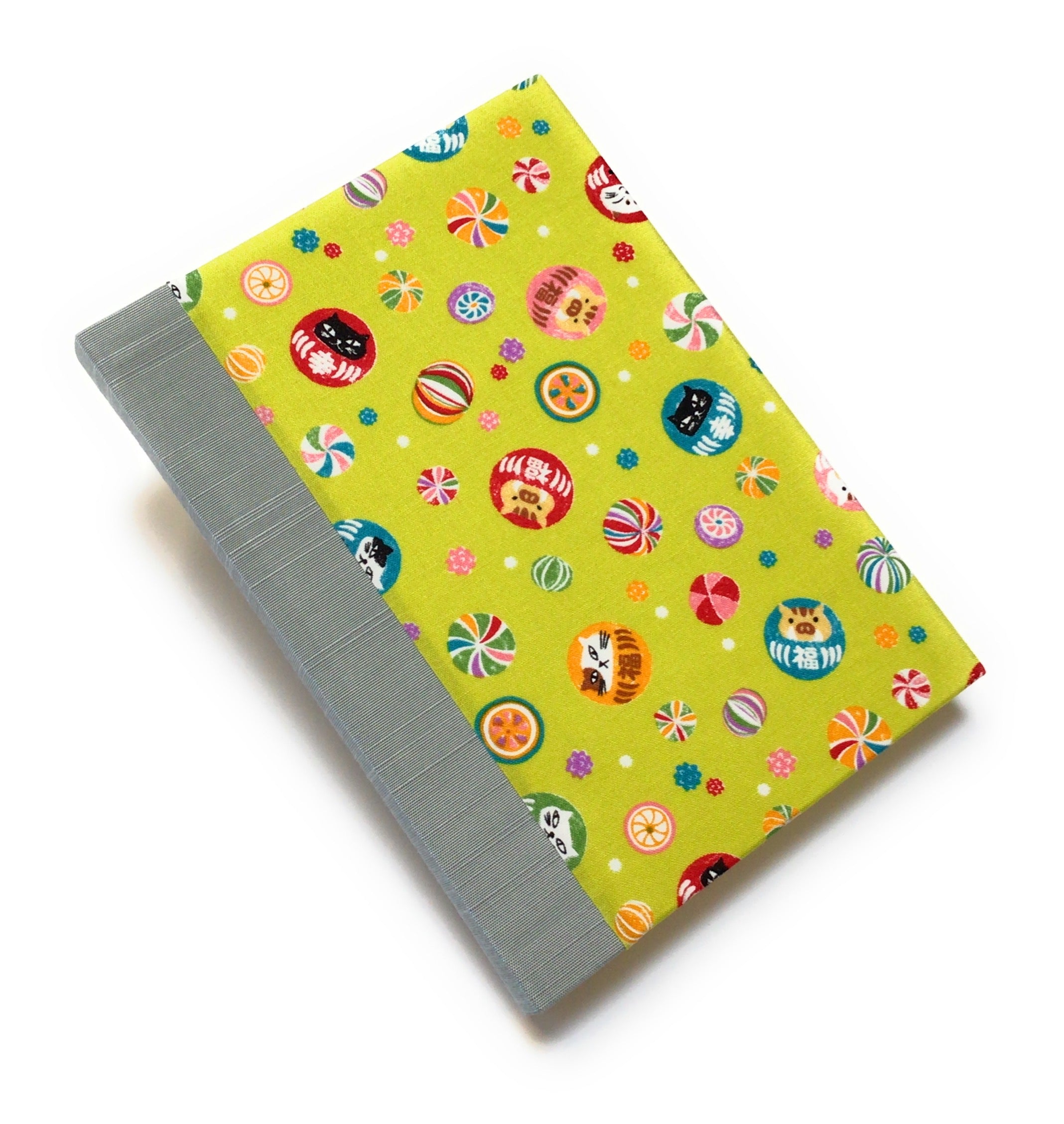 This handmade journal features a lively Japanese-inspired fabric cover adorned with lucky Daruma dolls, playful cat illustrations, and vibrant temari balls on a striking green background. The durable blue gray spine adds contrast, making it a perfect notebook for journaling, sketching, or note-taking. Designed for cat lovers and fans of Japanese aesthetics, this unique handcrafted journal is a stylish and functional keepsake.